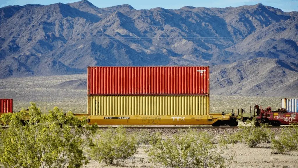 Rail freight shipment with stacked shipping containers traveling through the desert