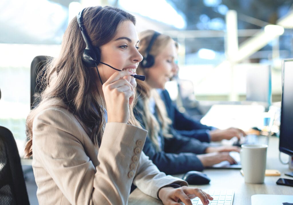 Female customer support operator with headset and smiling, with collegues at background